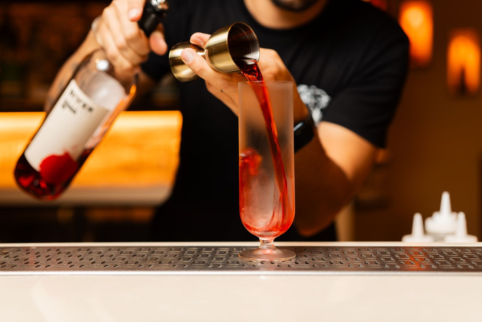 Gros plan sur un barman versant un cocktail rouge vif dans un verre au comptoir d'un bar.